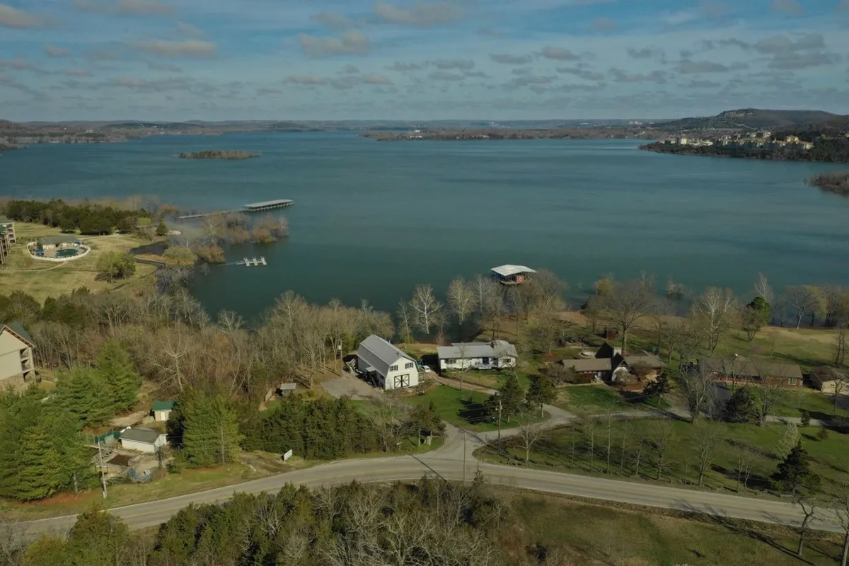 A panoramic view of the lake, shoreline, docks, surrounding greenery, and several houses. The image captures the peaceful ambiance and natural setting, with ample space for picnics, wildlife observation, or lakeside games.