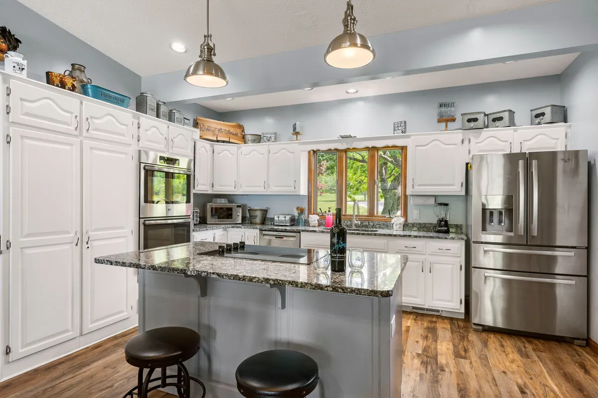 A modern, open-concept kitchen with a granite countertop, central island, stainless steel appliances, and a large window letting in natural light. The space is designed for both cooking and socializing, with plenty of room for group activities.