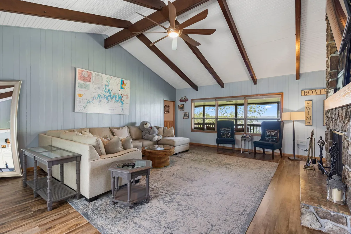 A spacious living room featuring a large sectional sofa, a wooden coffee table, a cozy fireplace, a map on the wall, and expansive windows overlooking the natural landscape outside. The room is filled with warm tones and inviting textures, creating a perfect space for family relaxation and gatherings.