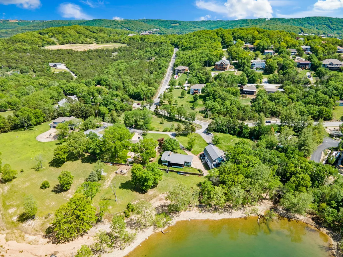 A scenic exterior shot capturing lush greenery, the edge of the water, residential structures, and a winding path or road. The area is ideal for hiking, exploring local trails, and enjoying scenic sunset views. The natural landscape invites guests to venture out beyond the shoreline.