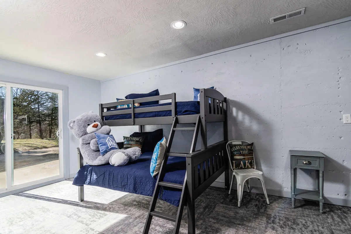 A cheerful, playful bunk bed room with a large teddy bear, decorative pillows, and a window that lets in plenty of light. The vibe is fun and welcoming, perfect for children or cousins enjoying sleepovers.