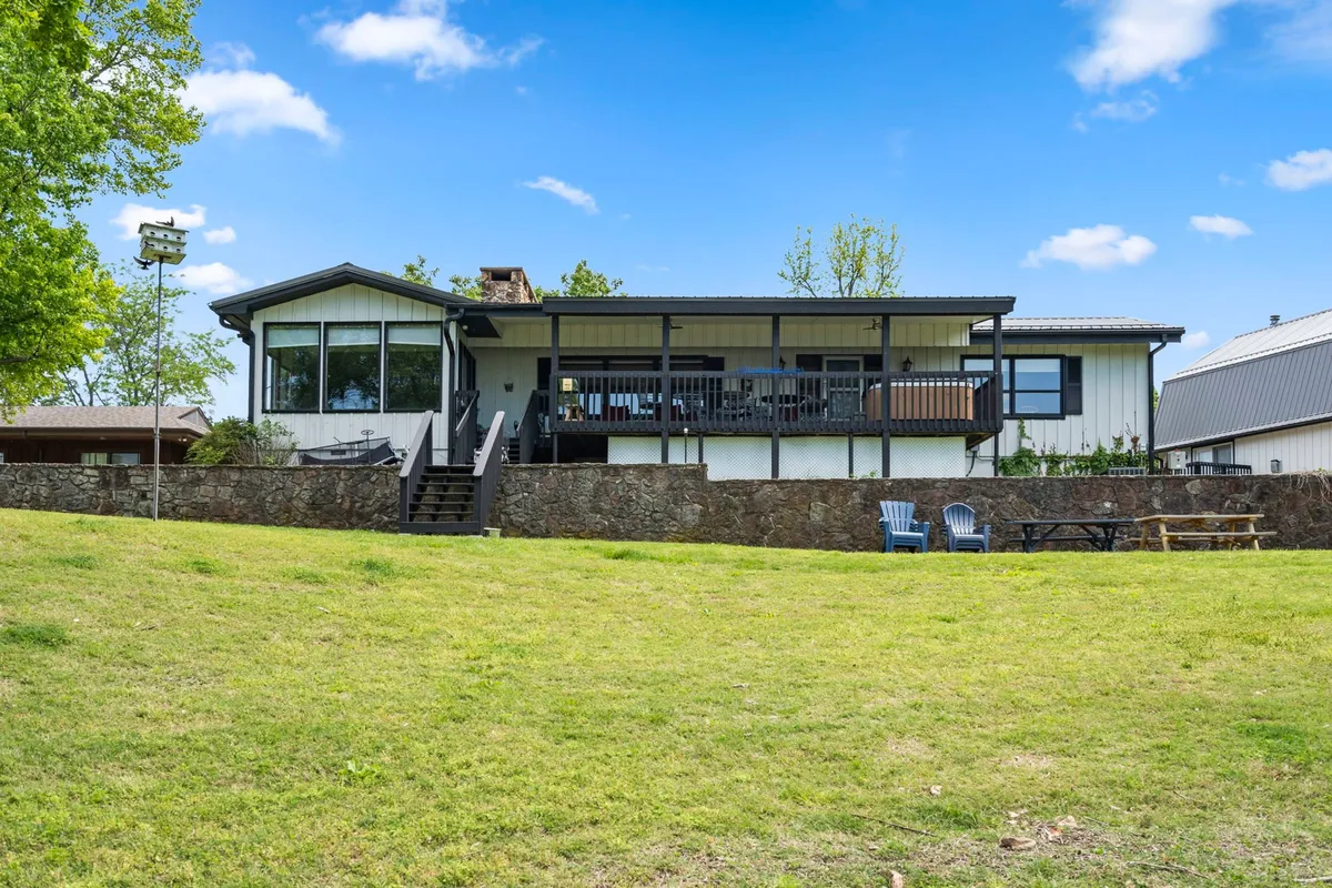 An exterior view of the house highlighting the large deck, spacious lawn, and picnic area. The open space is ideal for outdoor gatherings, relaxing, and safe play for pets and families alike.