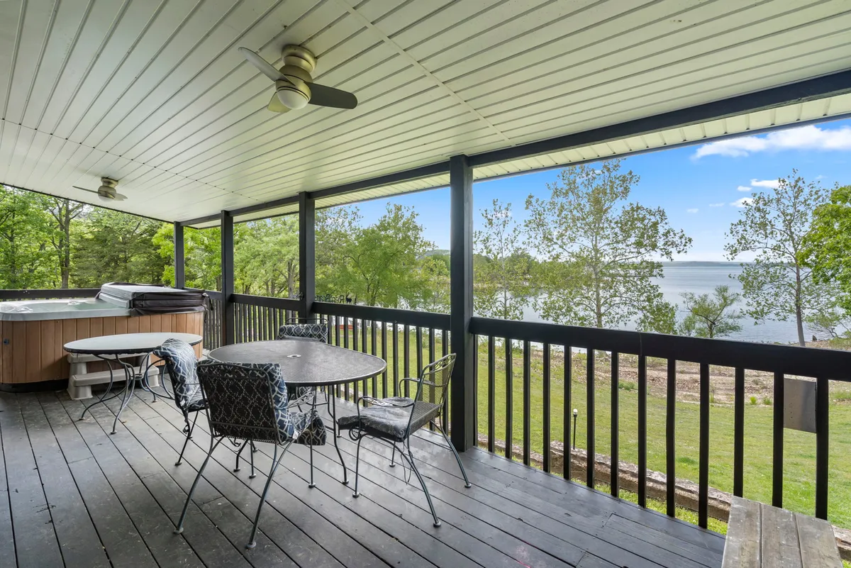 A serene lakeside deck featuring a private hot tub, dining table, and panoramic views of Table Rock Lake. The surrounding greenery and tranquil water create an idyllic setting for relaxation and outdoor gatherings.