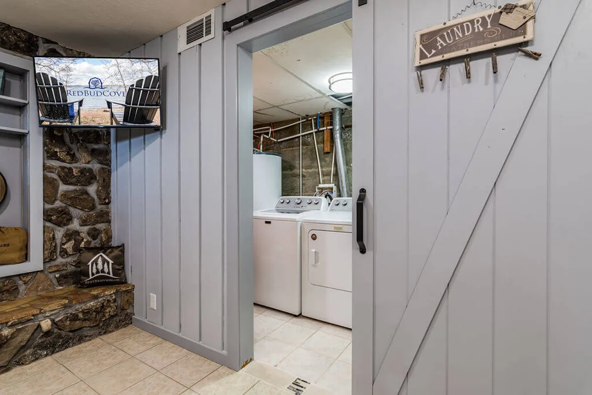 A functional laundry area featuring modern laundry machines, a stone wall, a mounted TV, and a decorative sign. The room feels practical yet inviting—a convenient amenity for longer stays or larger families.