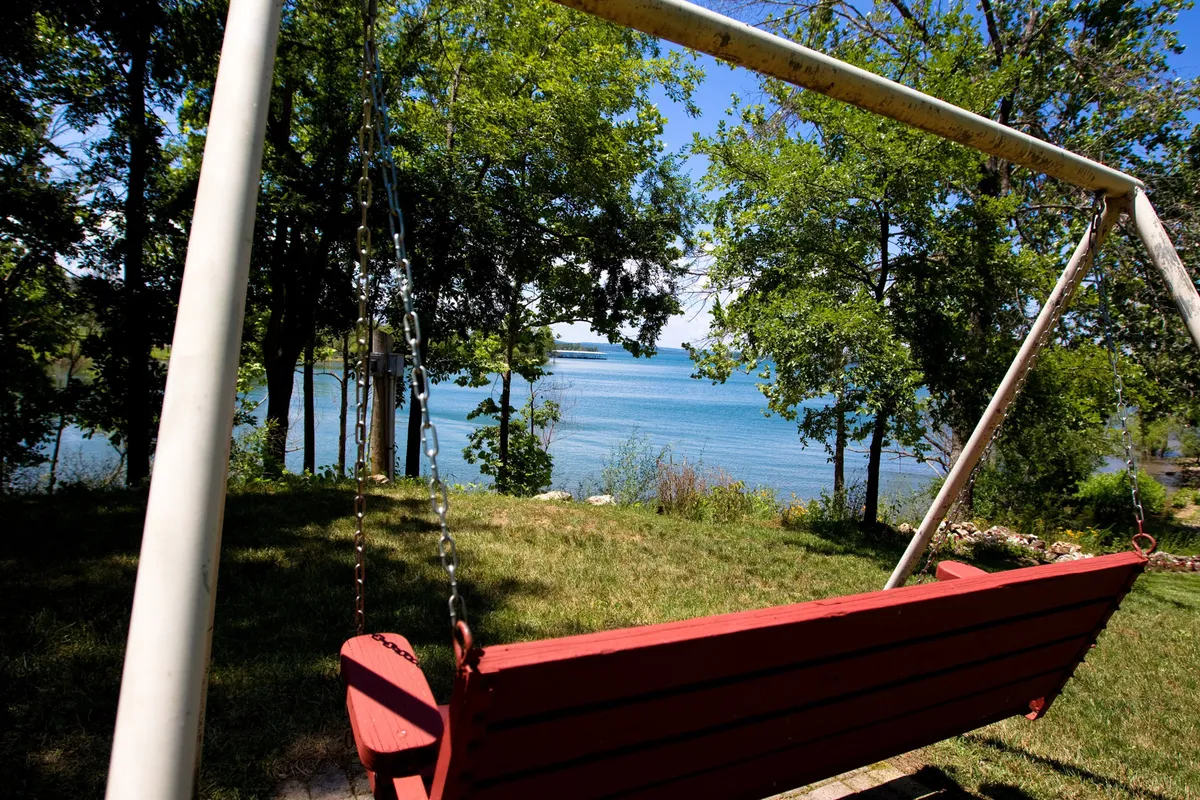 A red swing set beneath lush green trees, overlooking the tranquil lake. The image captures the peace of enjoying a quiet moment by the water, surrounded by nature.